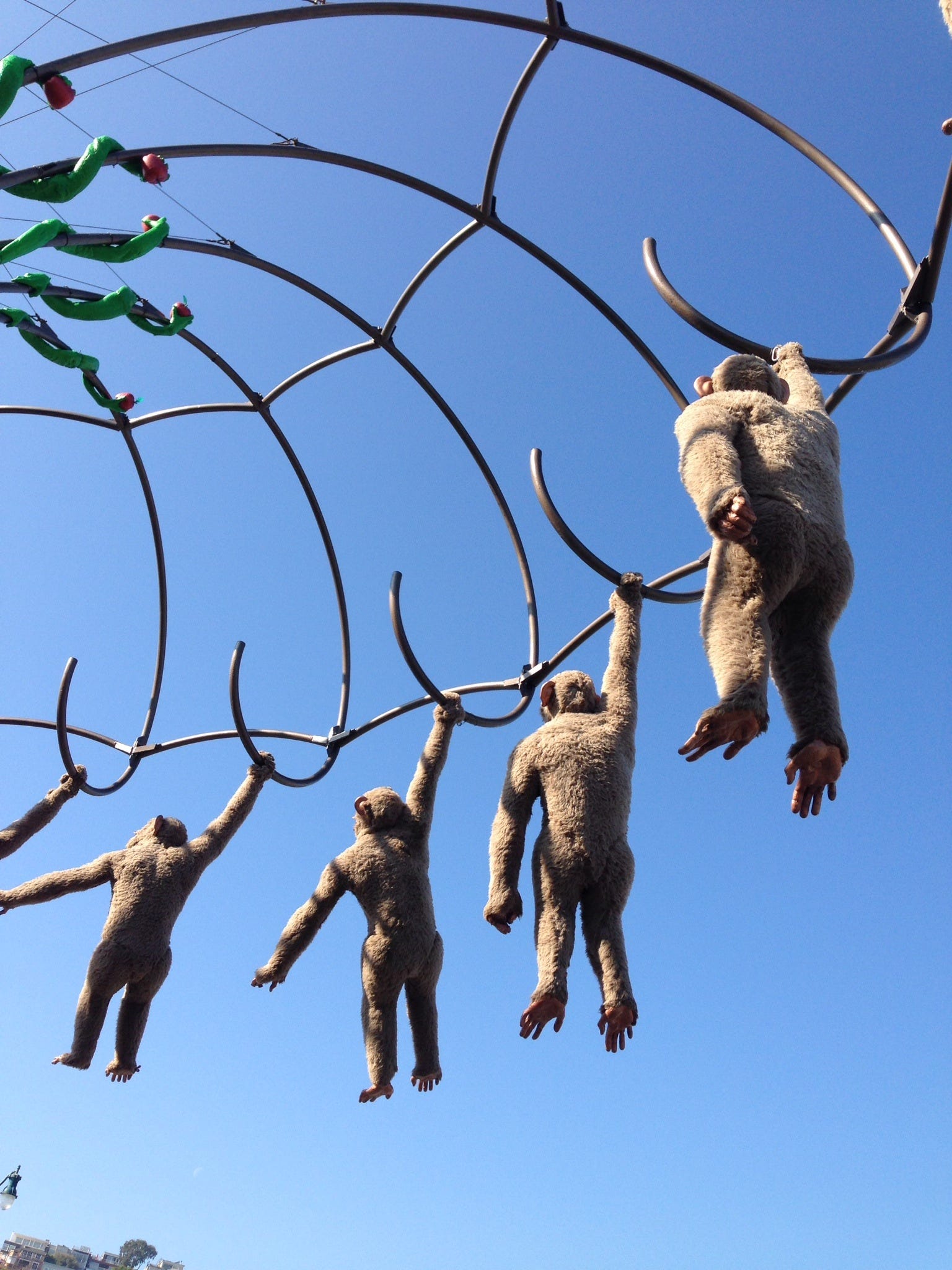 deep blue sky. moving sculpture of monkeys suspended in wire.
