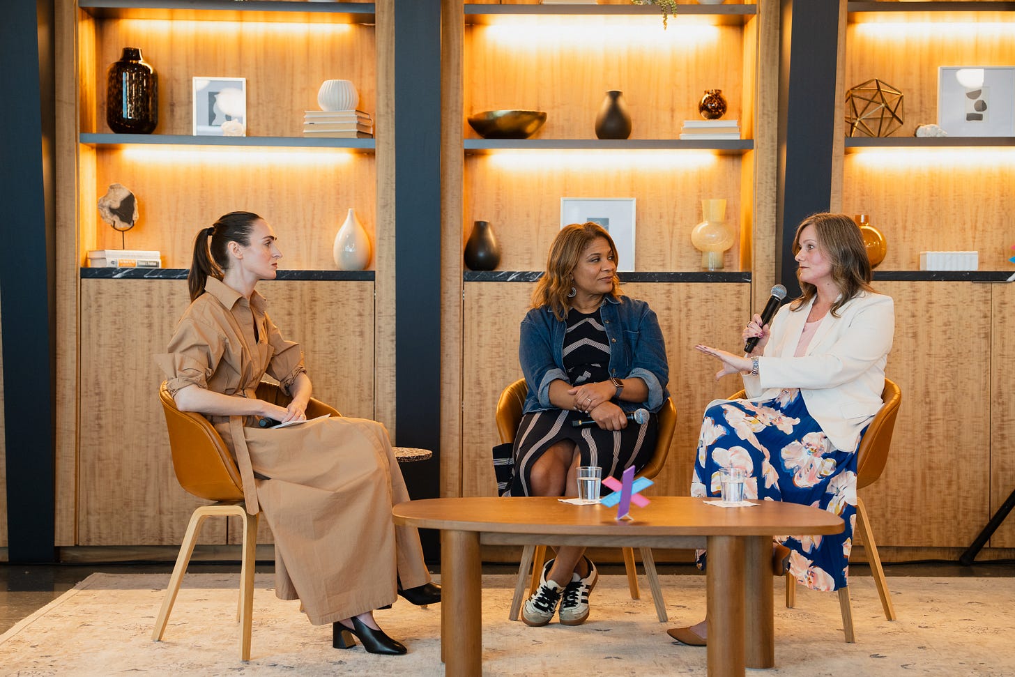 Jen Gerson, left, Fatima Goss Graves and Megan R. Holmes are seated behind a low table in front of wood shelving