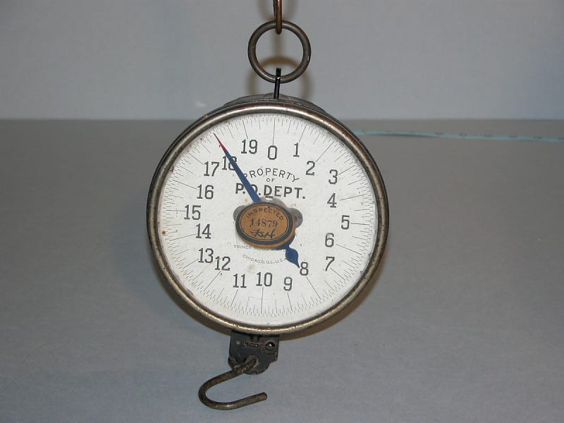 Photo of an old-time scale with a hook underneath to hang things to be weighed. Photo of an old-time scale with a hook underneath to hang things to be weighed.