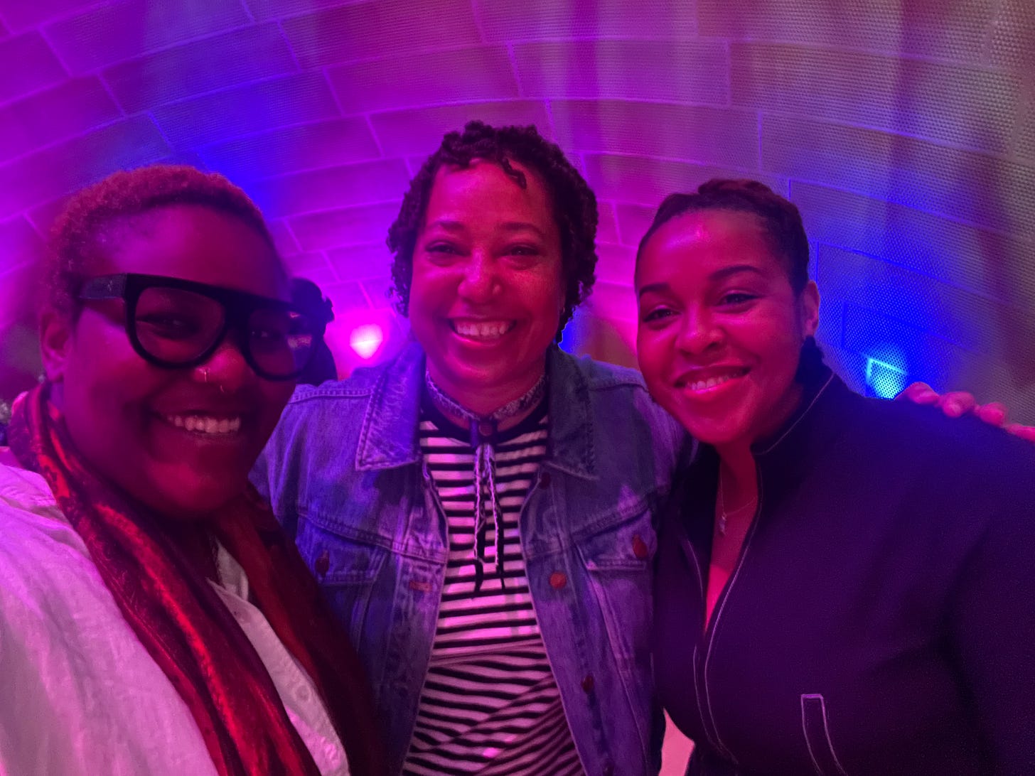 Three Black people taking a selfie against a white backdrop with blue and purple lights