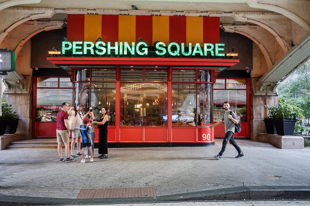 Street photo of Pershing Square Cafe with people gathered in front and one man walking past Street photo of Pershing Square Cafe with people gathered in front and one man walking past
