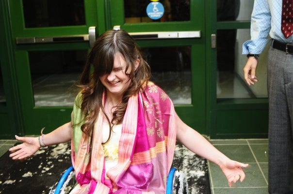 A white teen with brown long hair in her manual wheelchair, shaking off snow. A white teen with brown long hair in her manual wheelchair, shaking off snow.