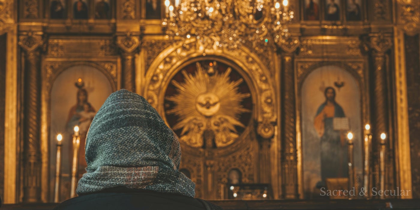 A person seen from behind sits alone in a softly lit, ornate church, facing a golden altar, creating a quiet and reflective atmosphere.