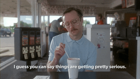 Movie gif. Aaron Ruell as Kip in Napoleon Dynamite plays with a straw in a styrofoam cup. He looks up at someone sitting across from him. Text, "I guess you can say things are getting pretty serious." Movie gif. Aaron Ruell as Kip in Napoleon Dynamite plays with a straw in a styrofoam cup. He looks up at someone sitting across from him. Text, "I guess you can say things are getting pretty serious."