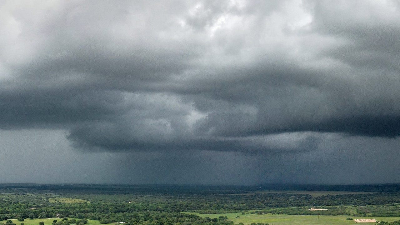 Dark rain clouds looming low over a green, wooded plain Dark rain clouds looming low over a green, wooded plain