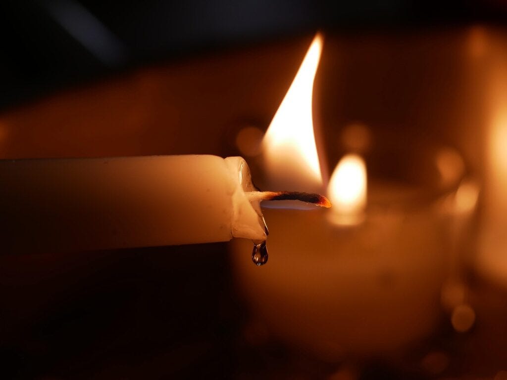 Close-up of a burning candle, with melted wax dripping, against a dark background.