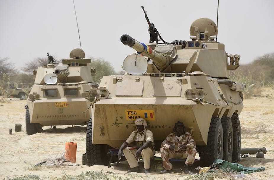 Men in military uniform, sitting in front an armoured vehicle