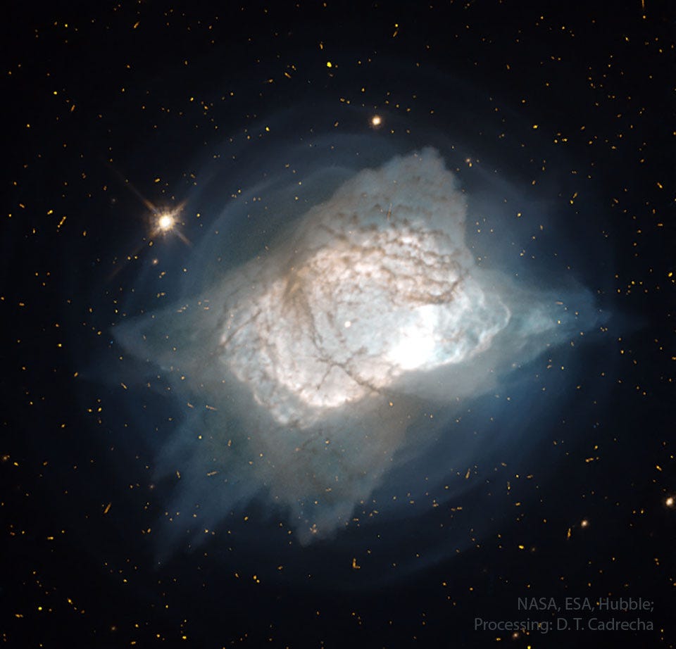 A starfield surrounds a bright nebula. The 
nebula is somewhat rectangular like a pillow
and is mostly white with brown filaments inside
and blue shells surrounding. 
Please see the explanation for more detailed information.
