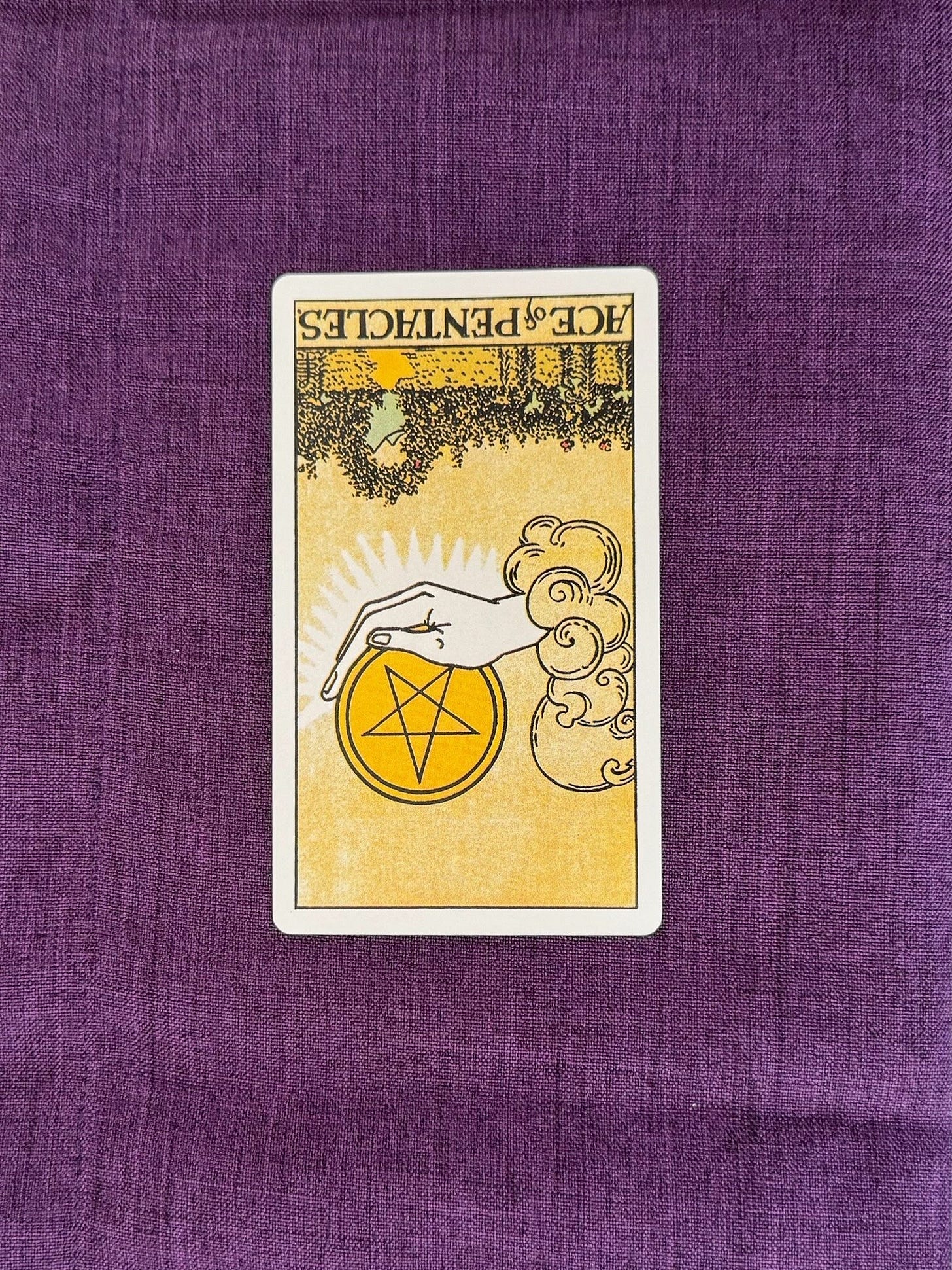 Tarot card upside down is the The Ace of Pentacles depicts a hand emerging from the clouds, holding a large coin on the cupped palm. The landscape is of a garden brimming with green grass and white lilies. A small path leads to an archway, wrapped in beautiful foliage and flowers and, beyond the arch, mountain peaks soar in the horizon. Tarot card upside down is the The Ace of Pentacles depicts a hand emerging from the clouds, holding a large coin on the cupped palm. The landscape is of a garden brimming with green grass and white lilies. A small path leads to an archway, wrapped in beautiful foliage and flowers and, beyond the arch, mountain peaks soar in the horizon.