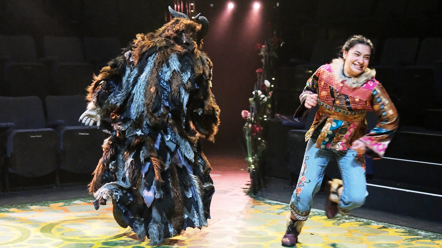 A shaggy beast dressed in many layers of pelts chases a Beauty clad in jeans and hiking boots.