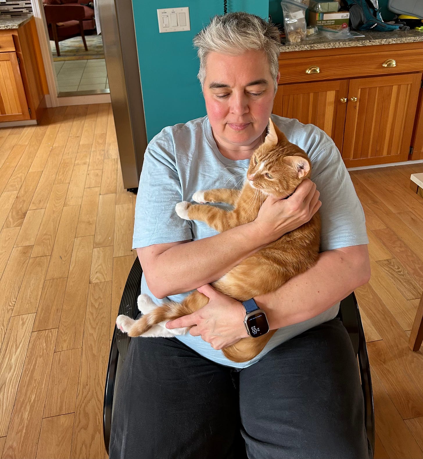 Naomi in wheelchair, holding Fezziwig cat who is looking a little impatient