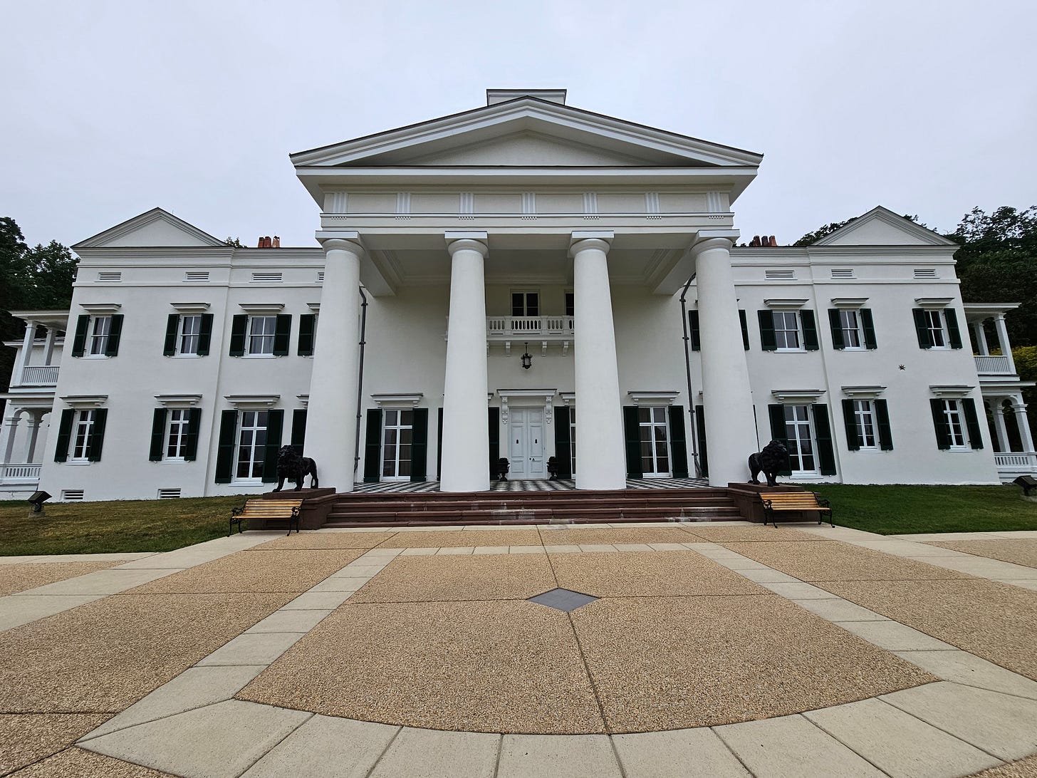Big white mansion with four large pillars, and black shutters.