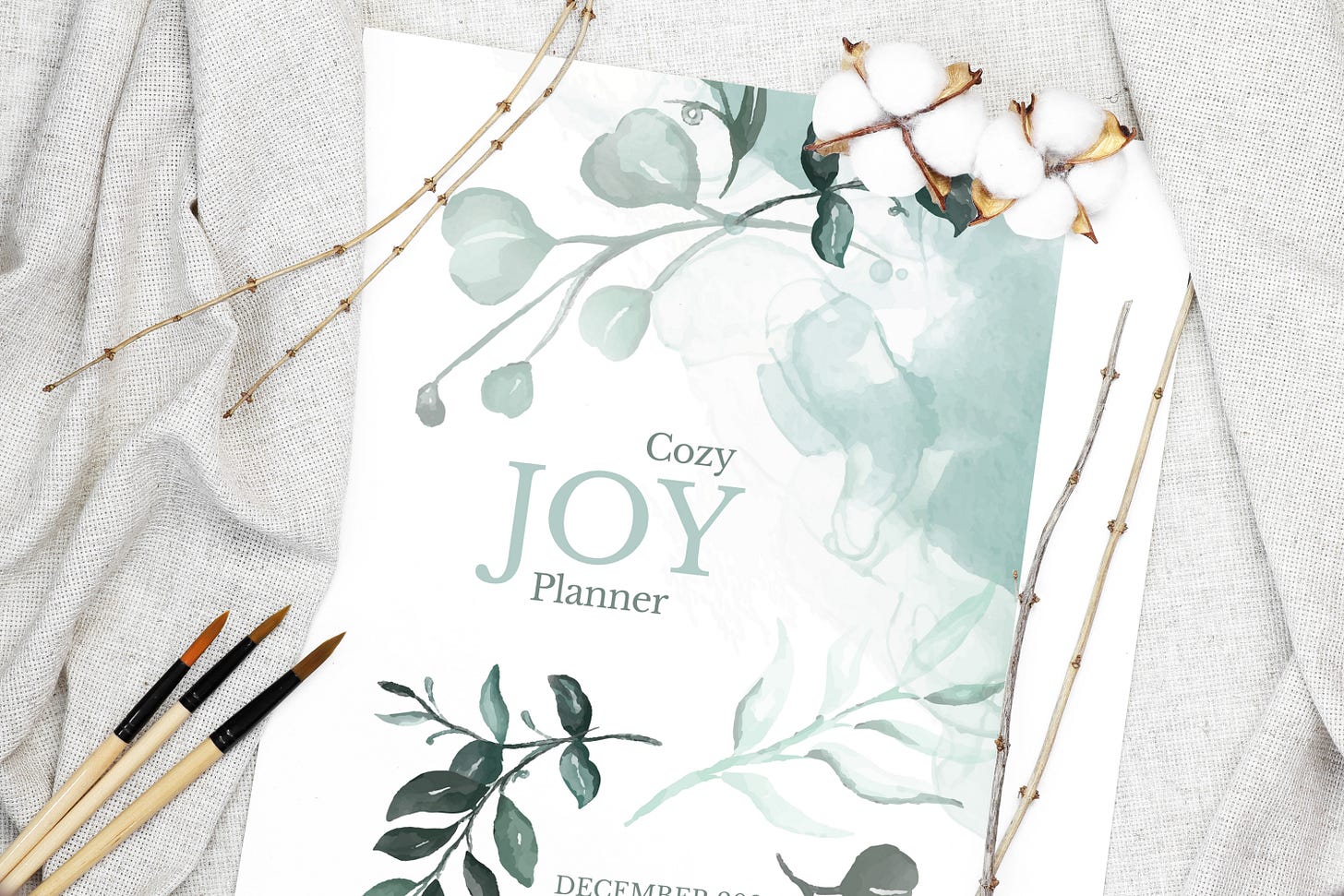 Cozy Joy Planner cover, surrounded by three brushes and two cotton flowers. Cozy Joy Planner cover, surrounded by three brushes and two cotton flowers.