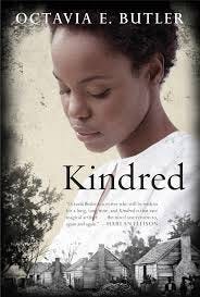 Cover of Kindred by Octavia Butler, featuring a black woman with a pained expression on her face, dressed in white, overlooking the foreground of a slavery-era farmhouse