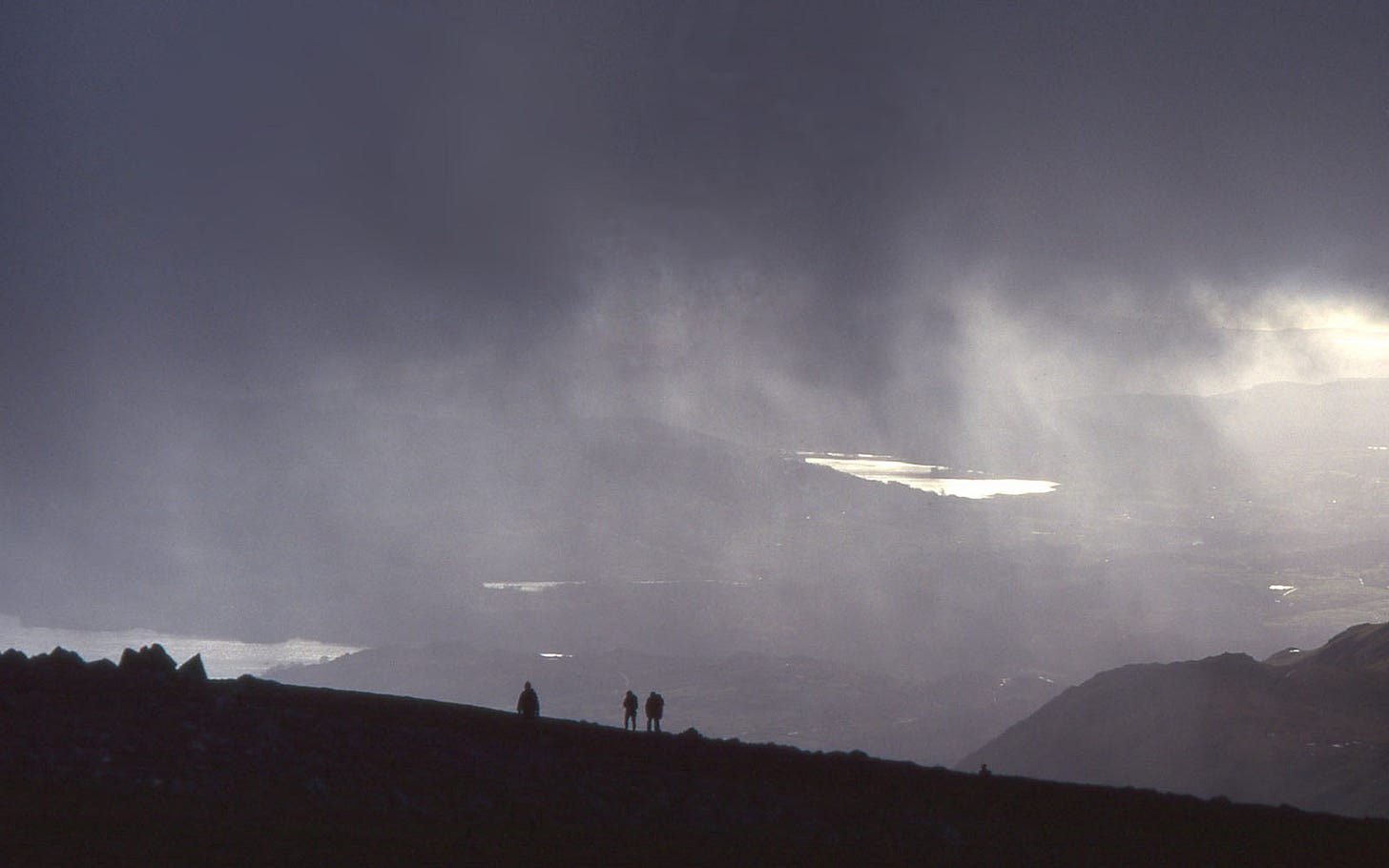 Hill walkers outlined against rain, misted lakes behind