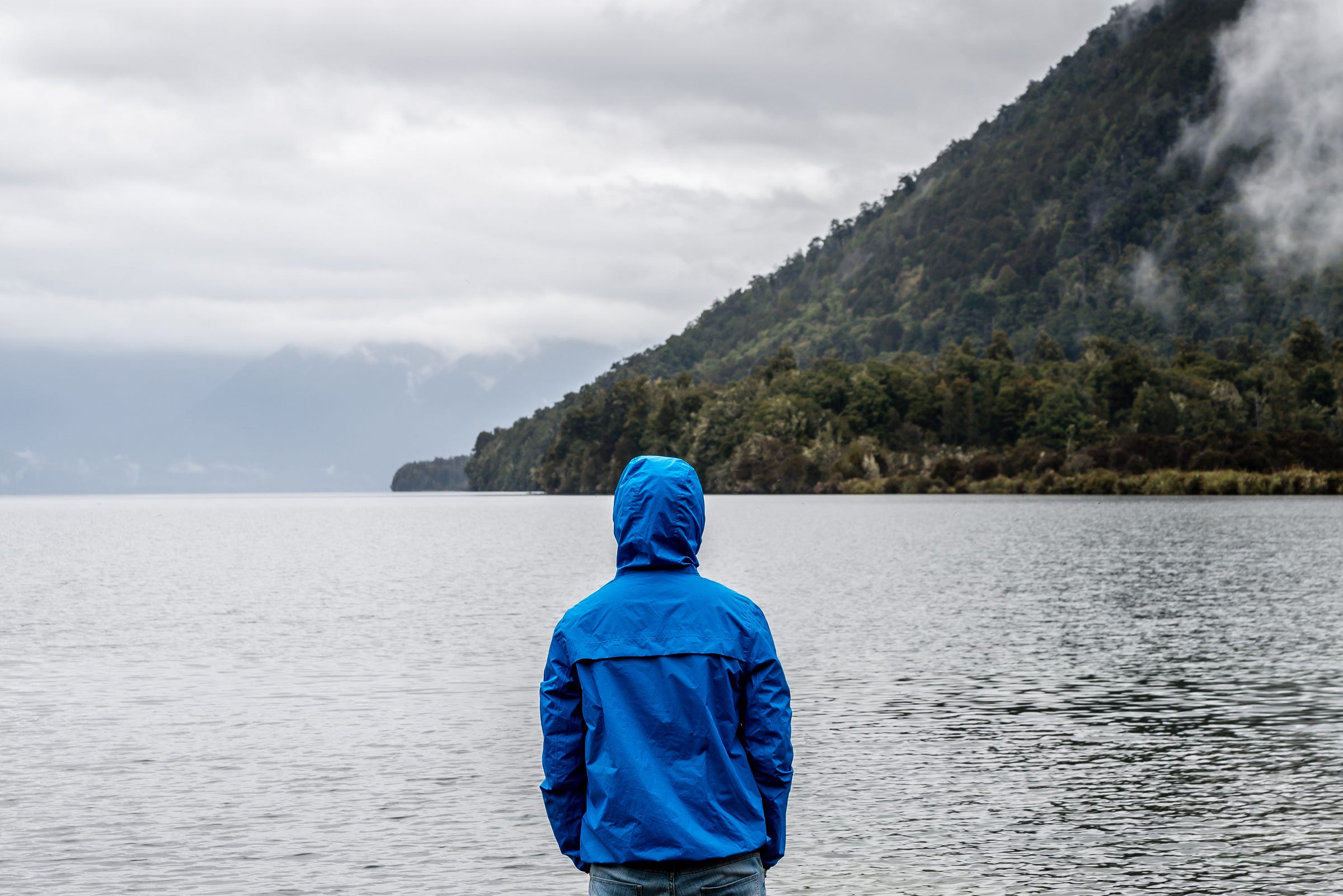 man standing by lake in blue coat looking out at the landscape