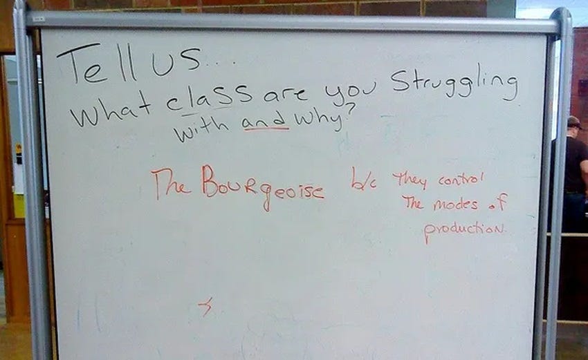 Photo of a whiteboard in a university common area with the question, in black marker, 'Tell us ... what class are you struggling with and why?' An answer in orange marker replies, 'The bourgeoisie, because they control the modes of production.' Photo of a whiteboard in a university common area with the question, in black marker, 'Tell us ... what class are you struggling with and why?' An answer in orange marker replies, 'The bourgeoisie, because they control the modes of production.'
