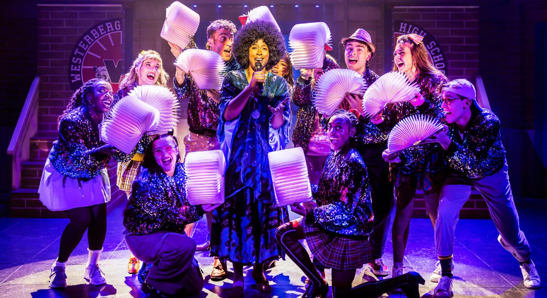 A group of people on stage holding fans against a woman singing A group of people on stage holding fans against a woman singing