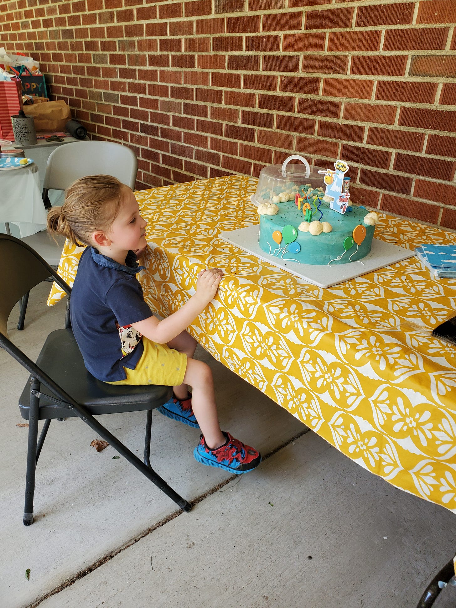 A 4-year-old smiles at sky blue cake covered in clouds and balloons.