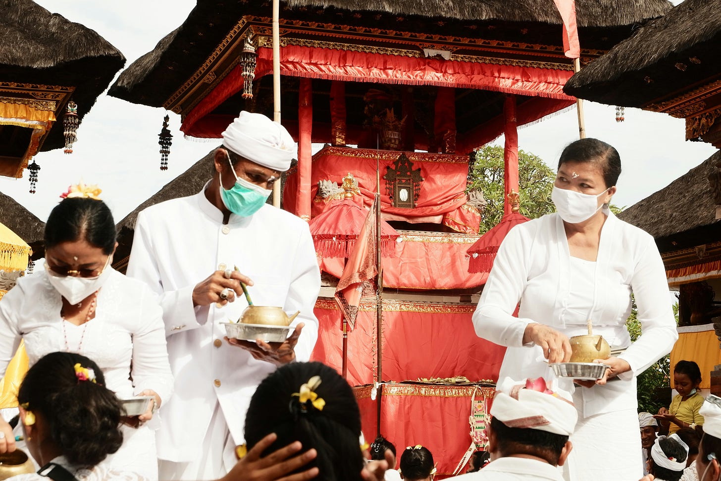 A Balinese ceremony during the pandemic showing masked people in ceremonial attire serving others A Balinese ceremony during the pandemic showing masked people in ceremonial attire serving others