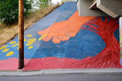 six photos in a grid #1 an installation of a larger than life cup of water pouring over an outdoor trail. #2 a B&W image of a woman at an altar with her arms raised. #3 a mural painted on a freeway under path showing a large hand on a blue and red background. #4 Dancers on a stage lying and kneeling under streams of fabric made to look like falling rain. #5 four dancers in a deep lunge surrounded by audience members sitting on chairs. #6 a tableau of three dancers taken outside on the edges of the Great Salt Lake, low hills are in the background.