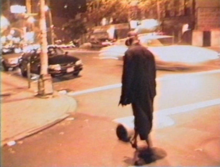 an image from the video piece Phat Free, depicting David Hammons kicking a bucket down a busy urban street