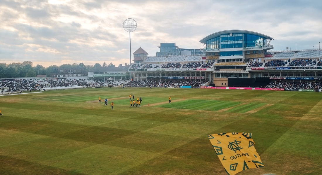 A cricket ground - Trent Bridge - with a green lawn and players on the pitch A cricket ground - Trent Bridge - with a green lawn and players on the pitch