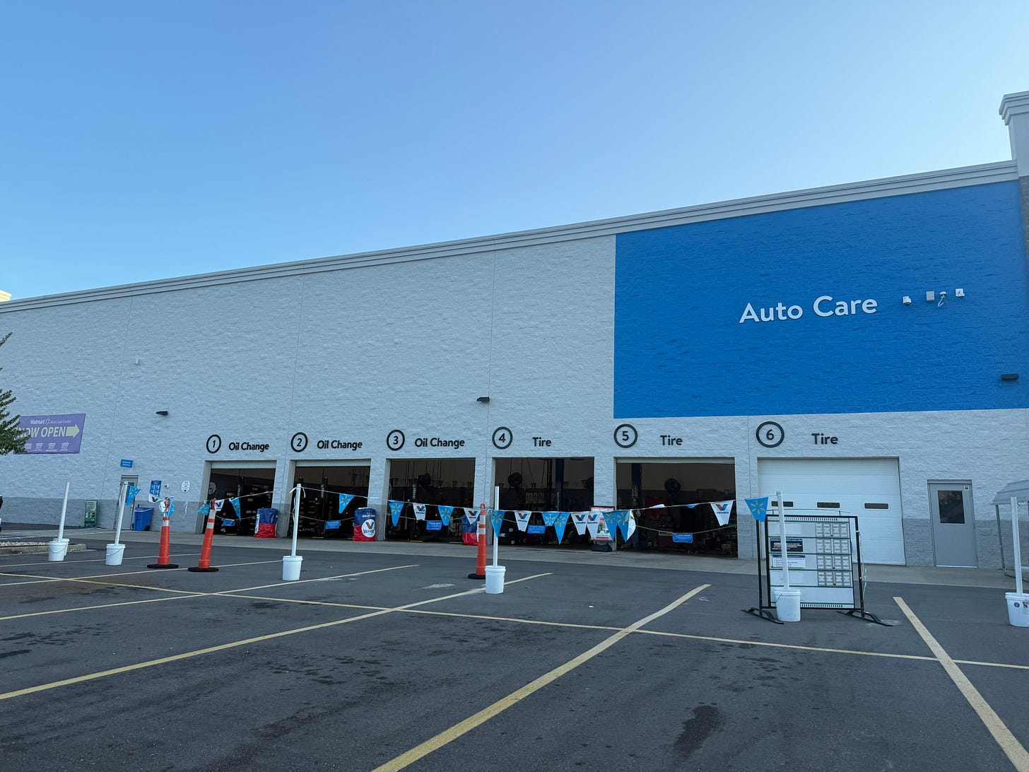 Walmart Auto Care service center exterior showing numbered service bays for oil changes and tire services, with blue and white corporate branding and red traffic cones in the parking lot