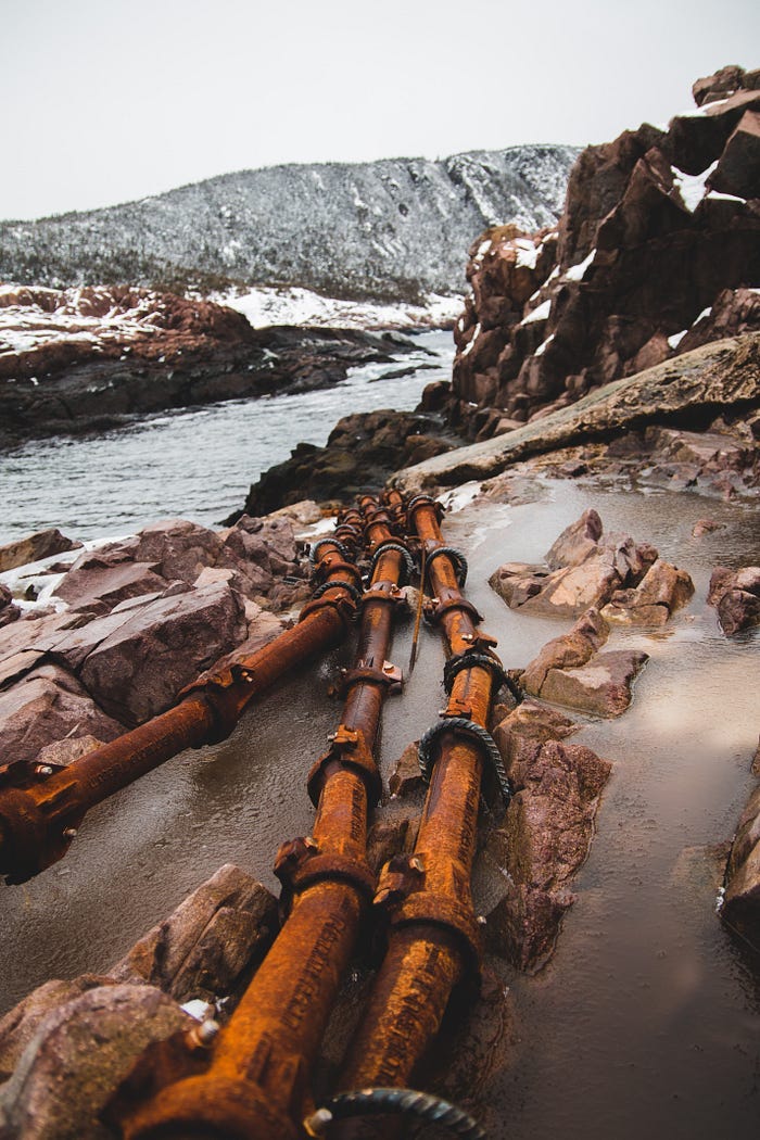 Old, rusty pipelines in the frozen winter wilderness. They stretch across the length of a rushing river, which could be contaminated if they should leak. Old, rusty pipelines in the frozen winter wilderness. They stretch across the length of a rushing river, which could be contaminated if they should leak.