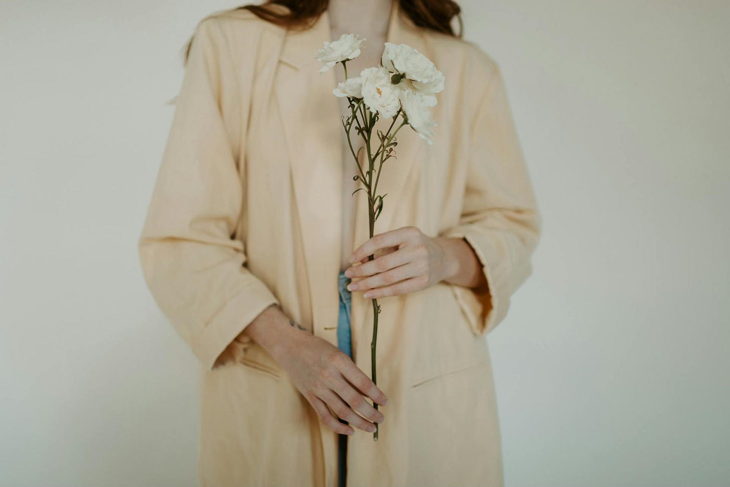 Cropped image of woman in beige holding white flowers.