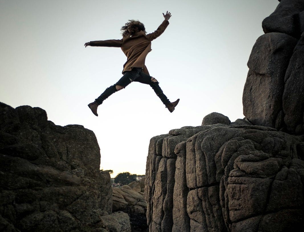 person jumping on big rock under gray and white sky during daytime person jumping on big rock under gray and white sky during daytime