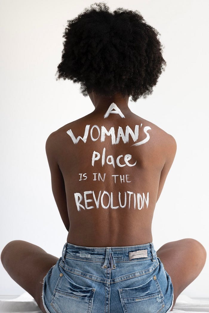 close up on a woman’s back with the words “a woman’s place is in the revolution” close up on a woman’s back with the words “a woman’s place is in the revolution”