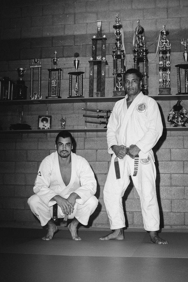 This may contain: two men standing next to each other in front of a wall with trophies on it This may contain: two men standing next to each other in front of a wall with trophies on it