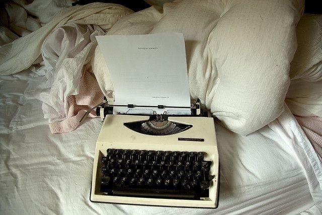 This may contain: an old fashioned typewriter sitting on top of a bed next to pillows and sheets