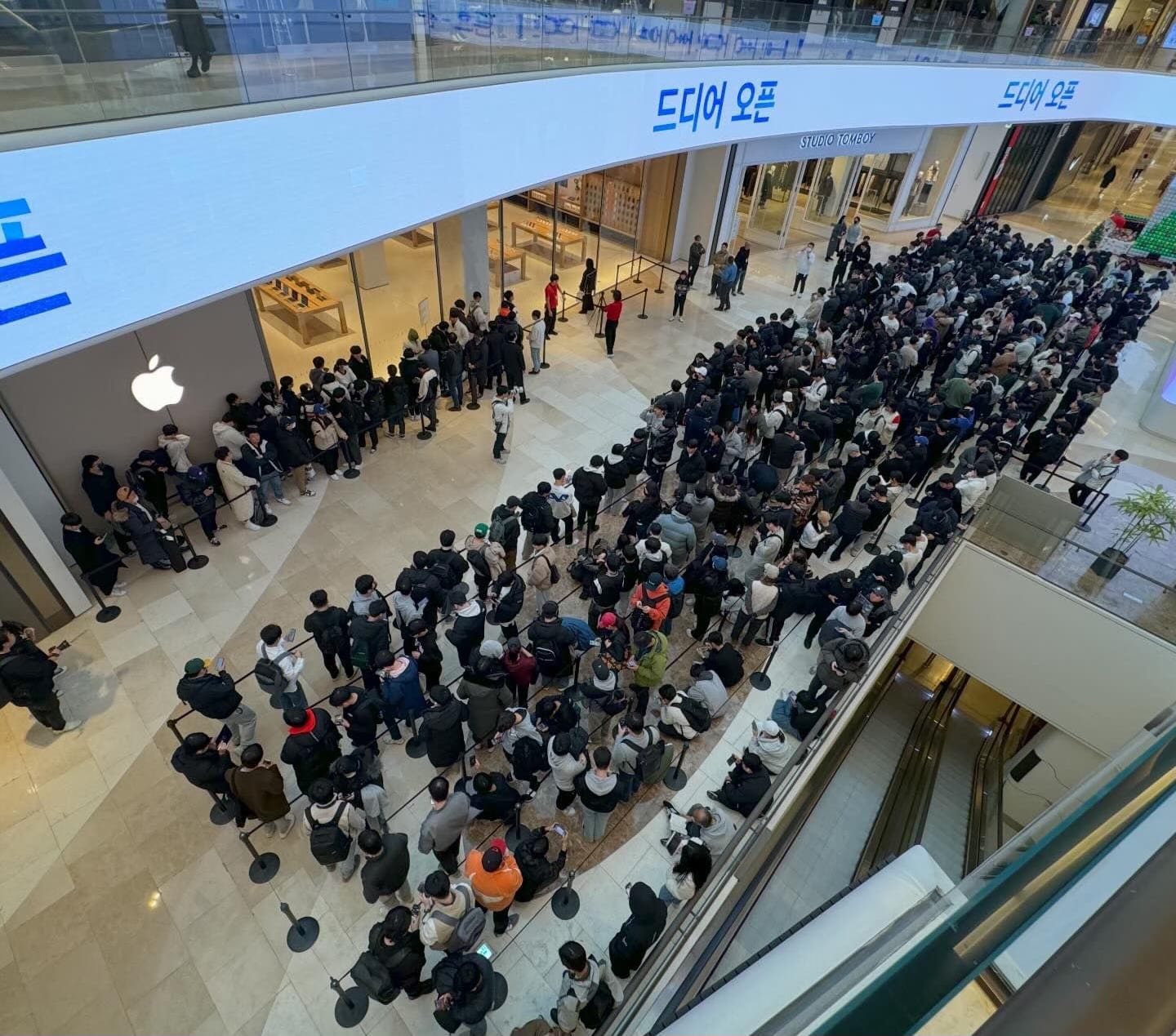 A large opening day crowd gathered outside Apple Hanam. The photo is taken from the second floor of the mall, looking down. A large opening day crowd gathered outside Apple Hanam. The photo is taken from the second floor of the mall, looking down.