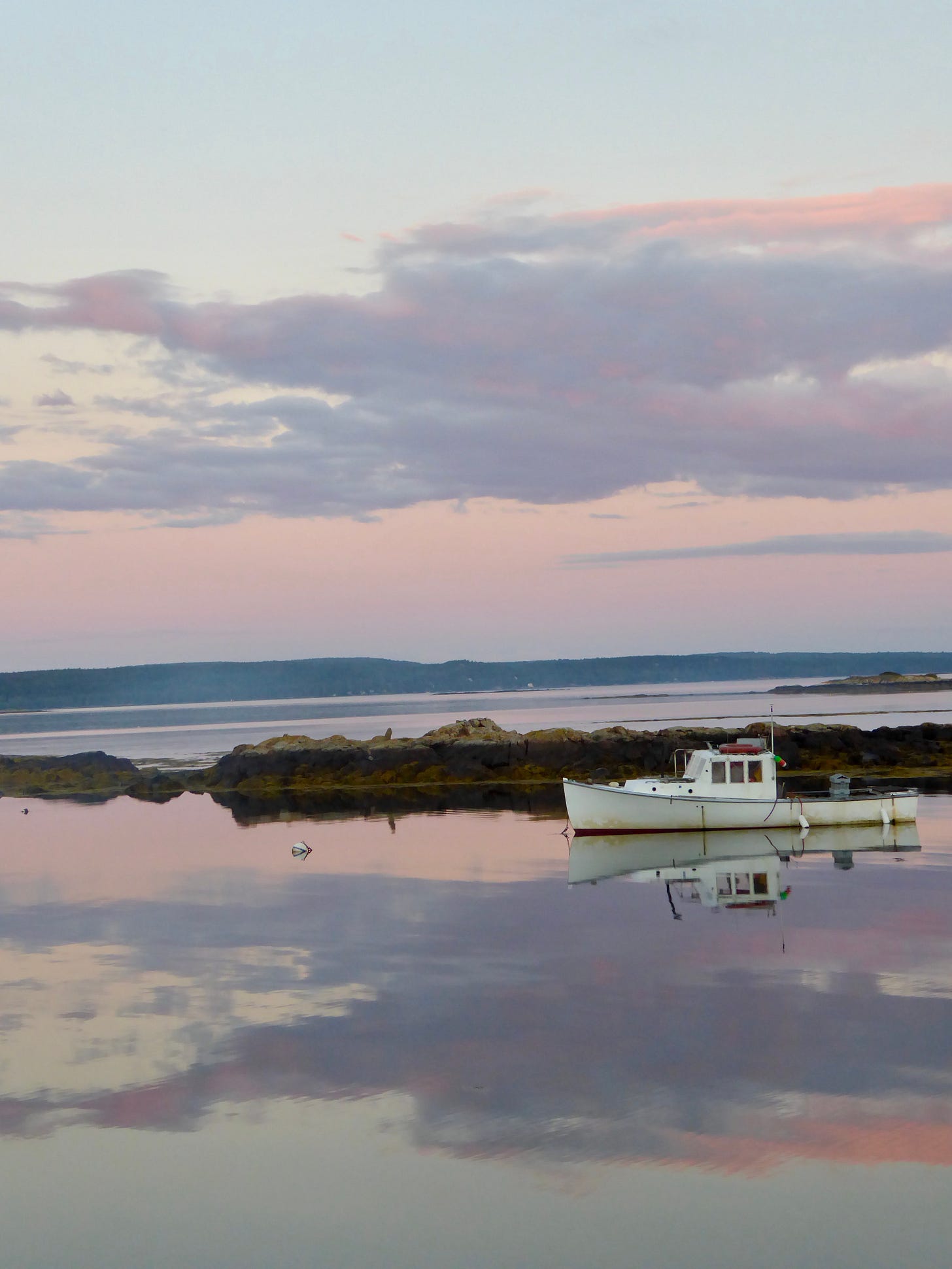 A purple pink sunset reflected on the sea with a lobster boat in the foreground.