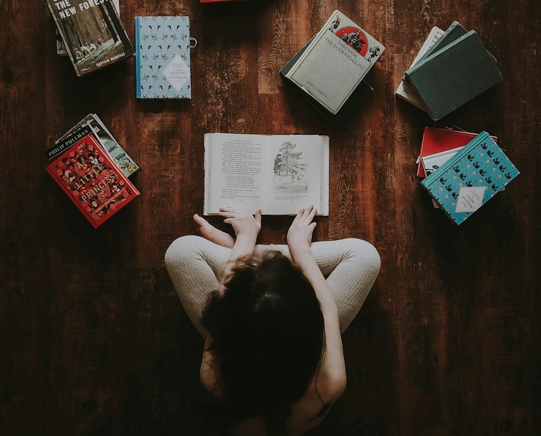 flat lay photography of woman sitting on brown wooden parquet flooring surrounded by books