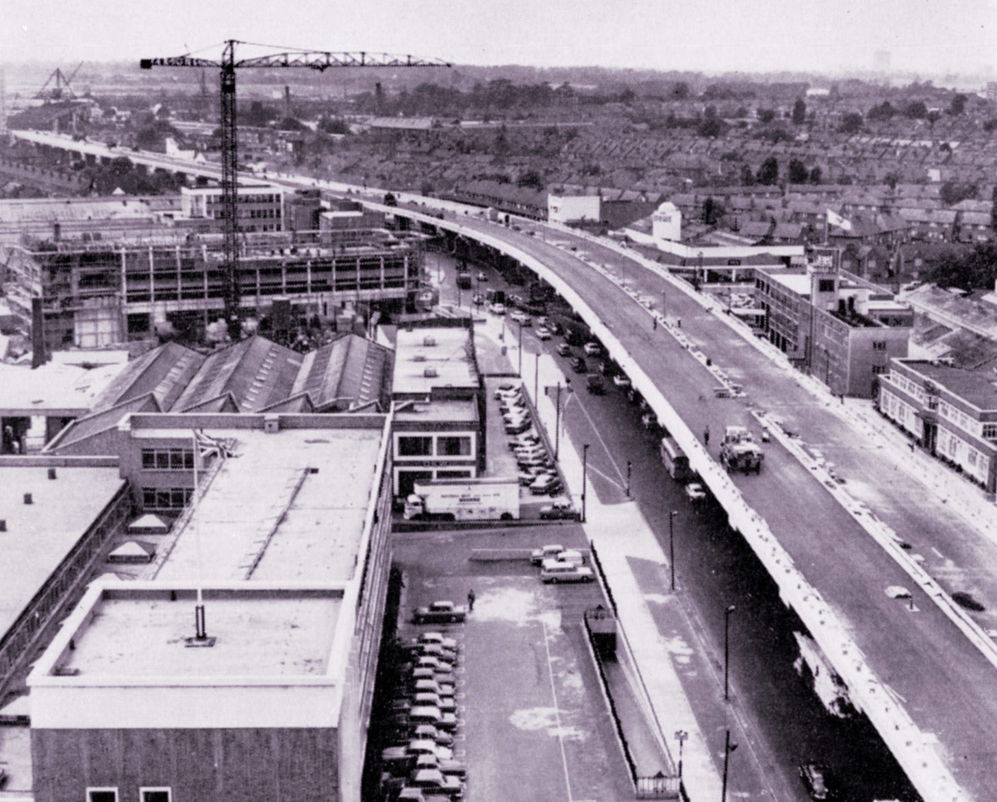 Black and white photograph showing a view of the M4 viaduct near Brentford nearing completion in the early 1960s. The picture is taken from a tall building and shows the road snaking away into the distance between factories and houses.