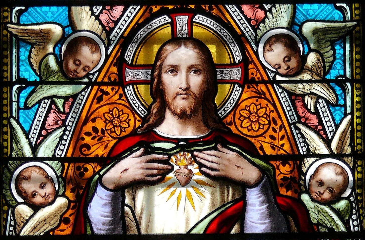 Detail of a nineteenth-century stained-glass window showing Jesus revealing his Sacred Heart, surrounded by angels and ornamental glasswork.