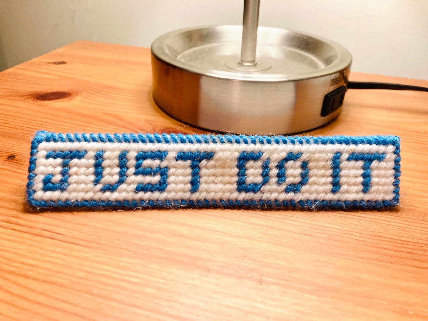 photo of a cross-stitch that says "Just Do It," sitting on a night stand