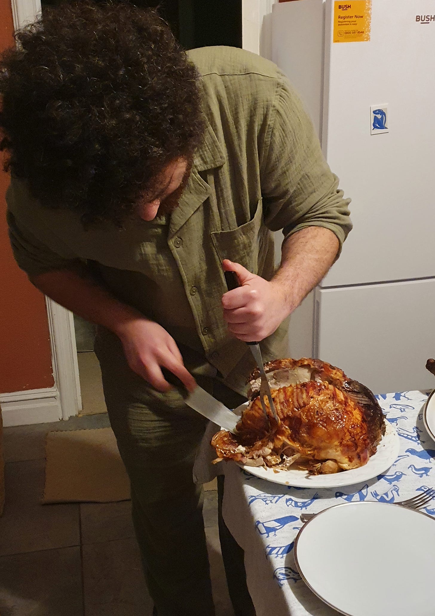 A man dressed in a khaki linen shirt and trousers carves a turkey