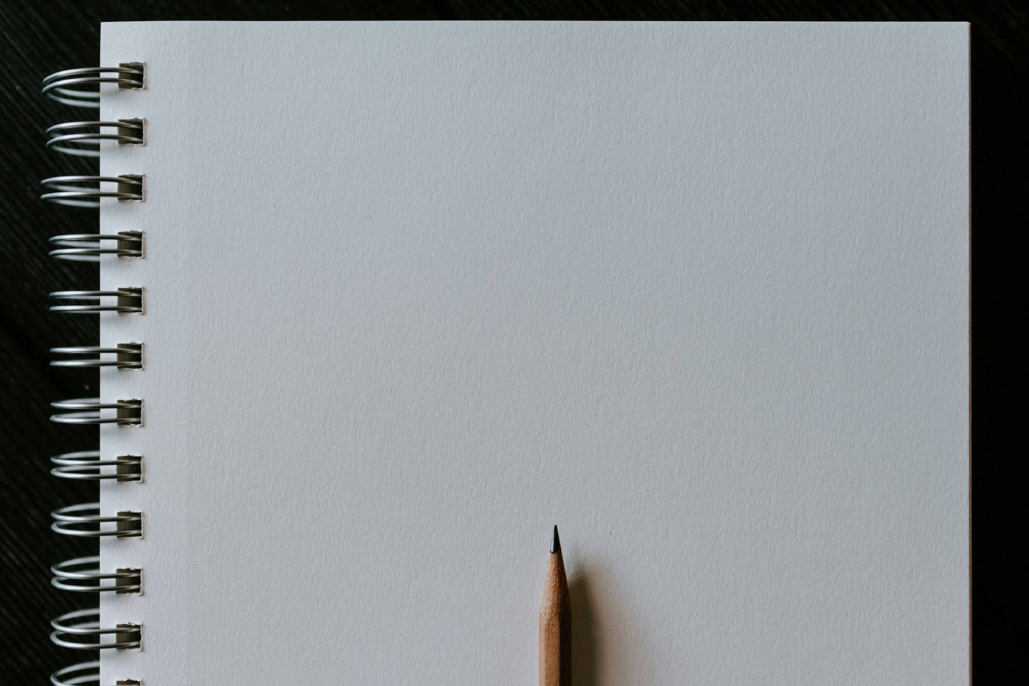 Spiral notebook open to a blank page. There is a pencil on the page.