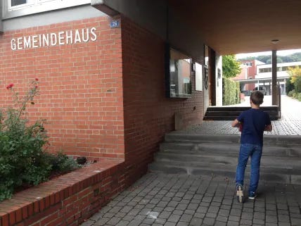 Small boy carrying large binder in front of town hall in a Swiss village.