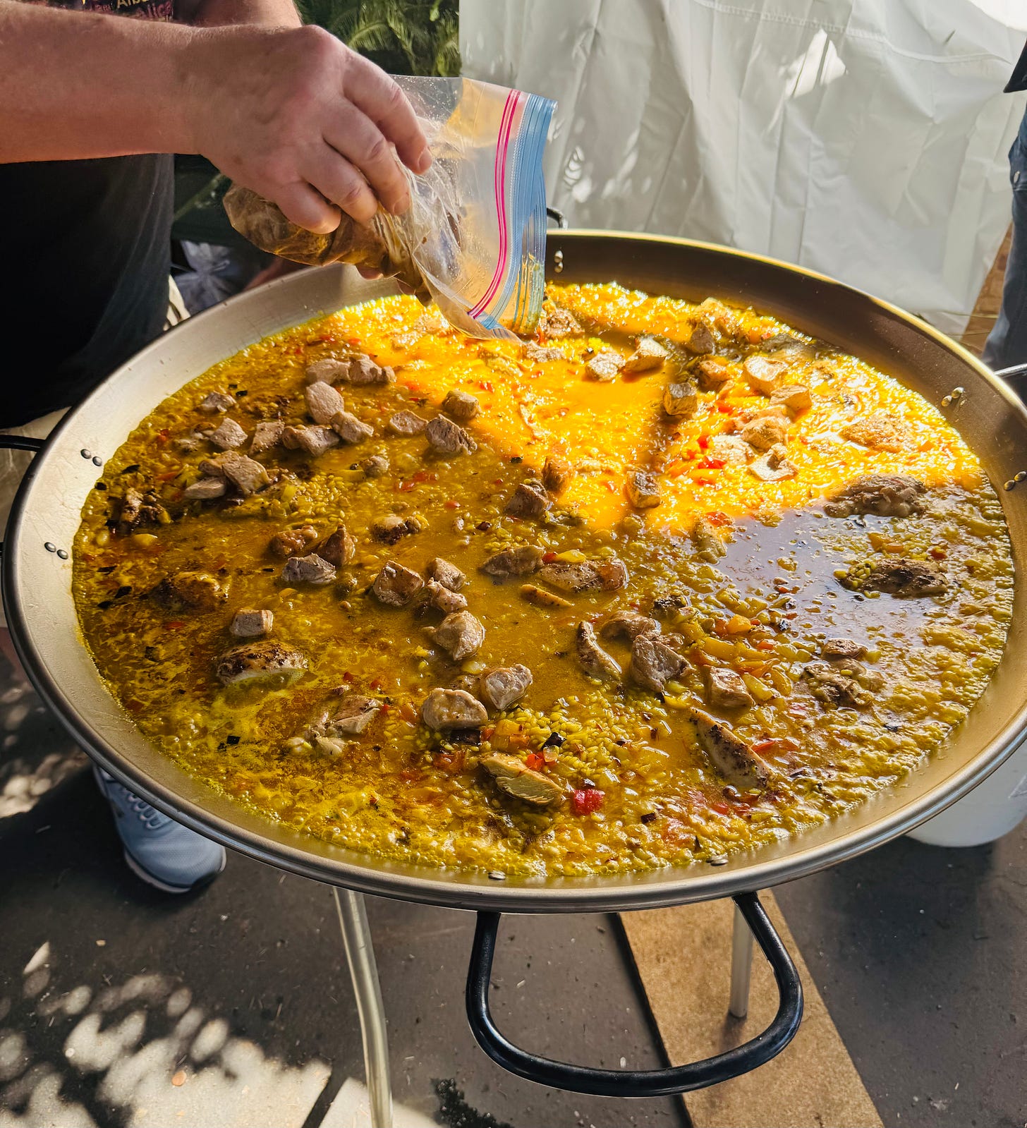 Pork loin being added to cooking paella