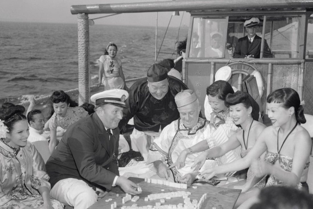 a group of people play mahjong aboard the Chinese junk Mon Lei, some in Chinese dress, all with amused faces a group of people play mahjong aboard the Chinese junk Mon Lei, some in Chinese dress, all with amused faces
