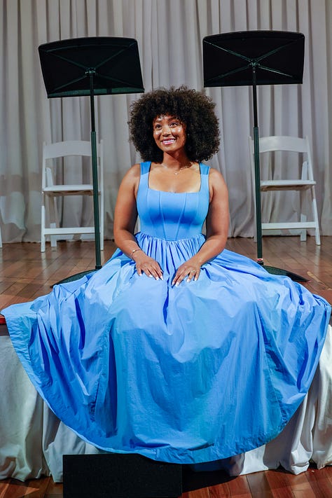 Dr. Mysia Anderson-White in a blue dress sitting on stage with music stands behind her.