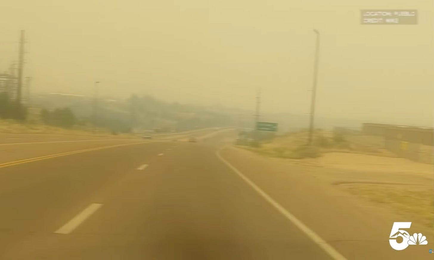 View through car windshield. Thick, suffocating smoke haze at ground level obscures visibility.