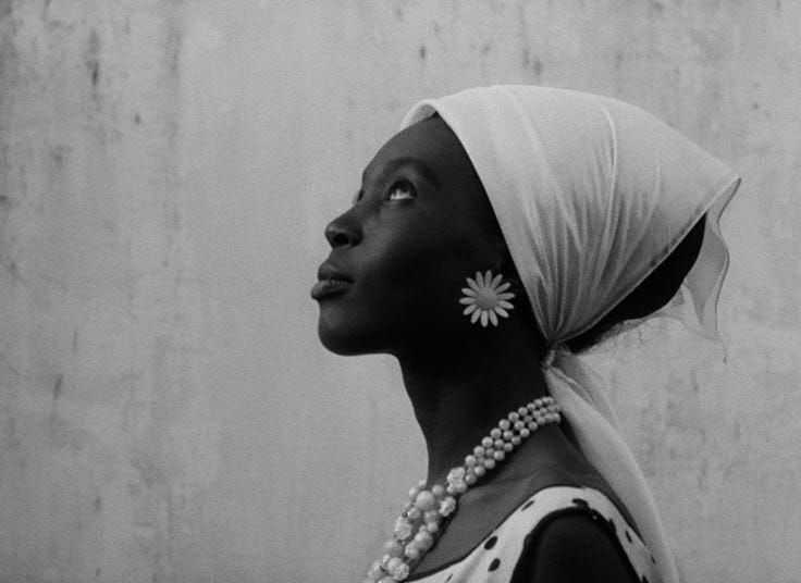This may contain: a woman with a white head scarf and pearls on her neck is looking up at the sky
