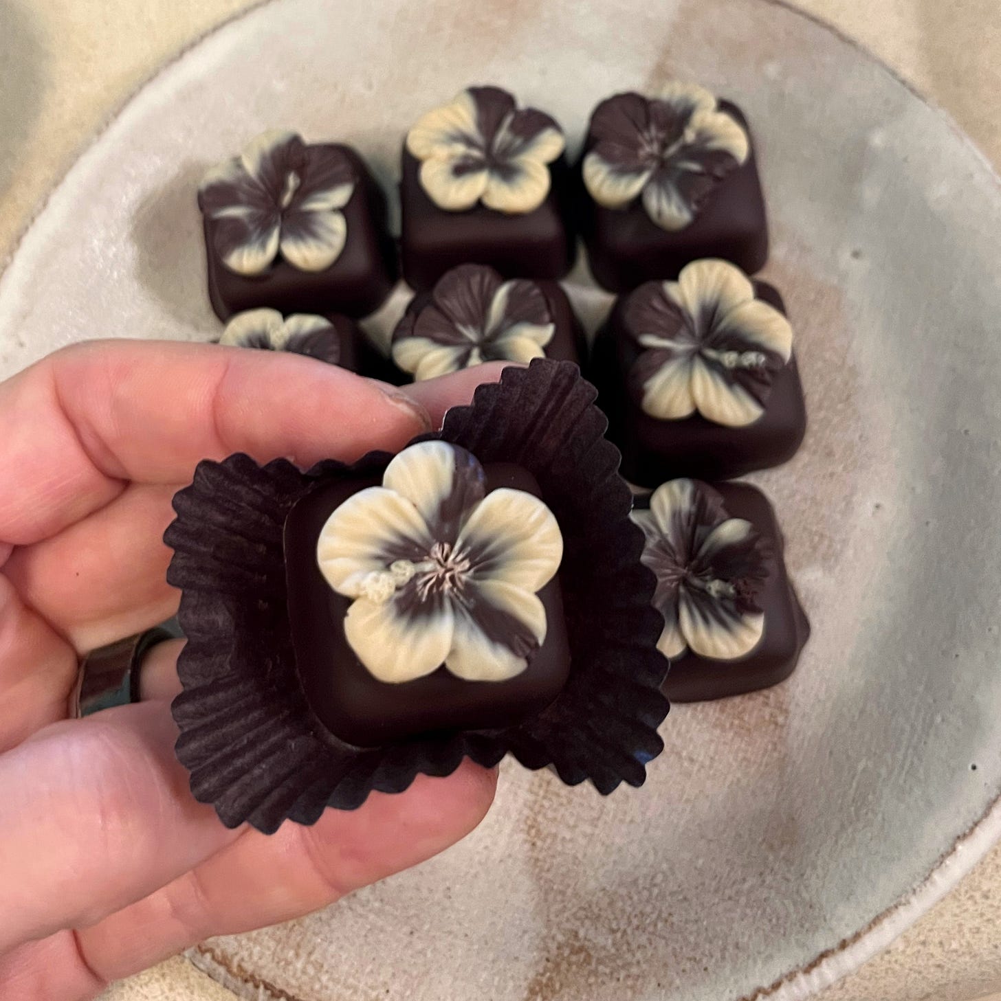 Hand holding a small chocolate bonbon with chocolate hibiscus flower decoration.