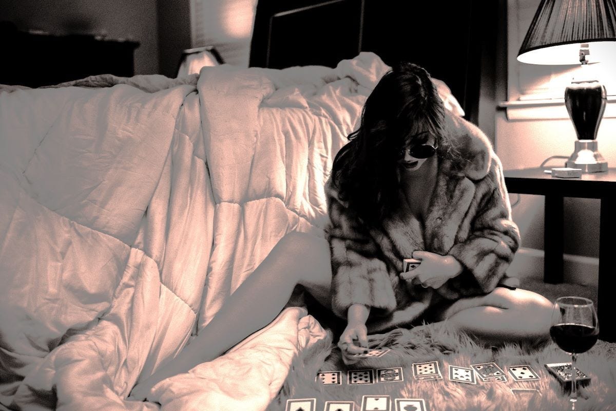 A woman playing cards with a glass of wine in her bedroom